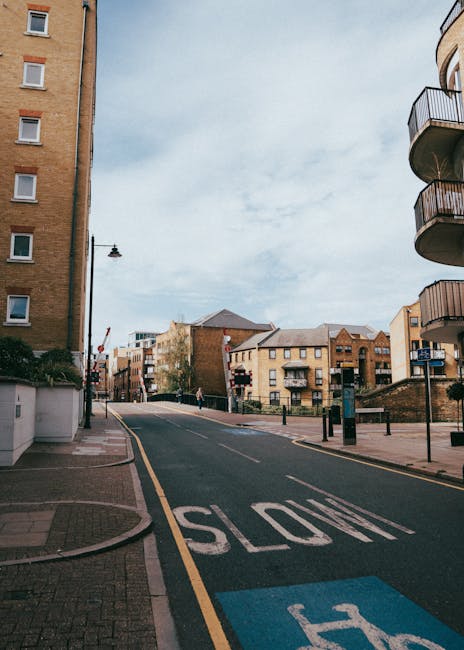 A street scene on Old York Road showing a row of terraced retail shops and apartments above, with red brick facades and large display windows. In front of the shops, a line of parked cars, including b